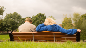 Ein älterer Mann sitzt mit einer jüngeren Frau auf einer Parkbank. Die Rückansicht wurde fotografiert.